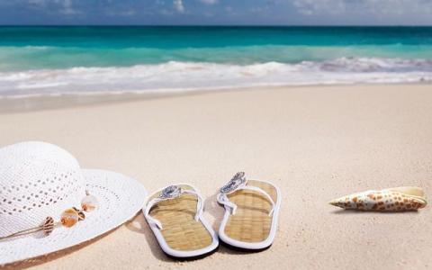 Urlaubsbild mit Strand, Meer, Badeschlapfen und Sonnenhut